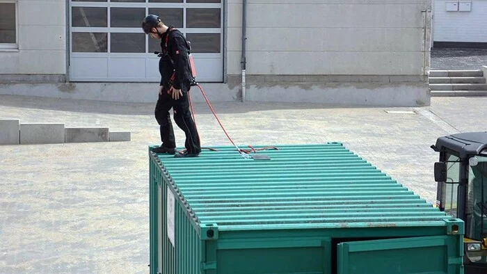 Foto eines zur Absturzsicherung angeleinten Arbeiters auf einem Frachtcontainer.