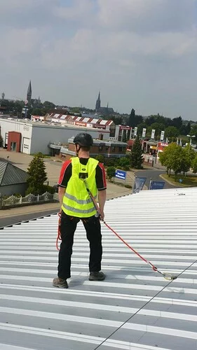 Foto von einem gegen Absturz angeleinten Dacharbeiters, der eine Warnweste mit integriertem Auffanggurt trägt.